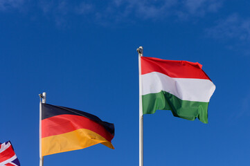 Colorful flags of Germany and Hungary waving under a bright blue sky on a sunny afternoon