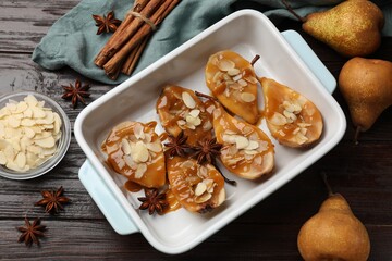 Delicious pears with caramel sauce, almond flakes and spices on wooden table, top view
