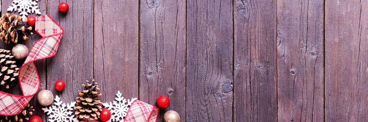 Christmas corner border of red and brown ribbon, snowflakes, baubles and pinecones. Above view on a dark wood banner background. Copy space.