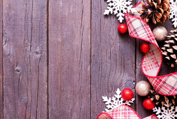 Christmas side border of red and brown ribbon, snowflakes, baubles and pinecones. Overhead view on a dark wood background. Copy space.