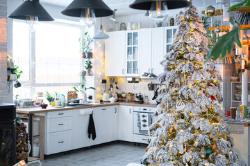 Christmas decor in white kitchen, modern rustic interior with a snowy Christmas tree and gold fairy lights. New Year, Christmas mood, cozy home. 