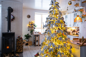 Festive white modern interior of house is decorated for Christmas and New Year in loft style with black stove, fireplace, Christmas tree. Potted plants, firewood in the woodpile