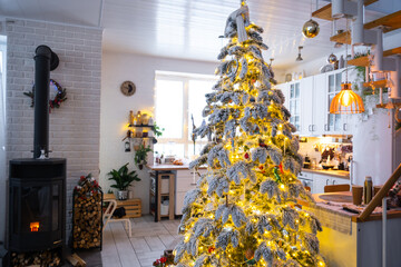 Festive white modern interior of house is decorated for Christmas and New Year in loft style with black stove, fireplace, Christmas tree. Potted plants, firewood in the woodpile