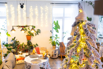 Festive Christmas decor in living room in a green house in the loft style with a retro wooden lampshade with a snowy Christmas tree and fairy lights. New Year, Christmas mood, cozy home.