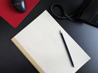 The notebook and pencil are on the office desk next to the phone and computer mouse.

