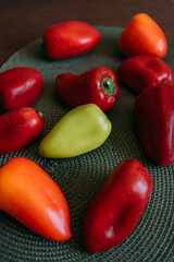 Fresh red and orange bell peppers with one green pepper on a green woven placemat, perfect for healthy cooking, food preparation, or rustic kitchen themes, showcasing natural ingredients