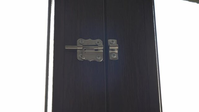 A close-up of a security latch on a door leading to a garden, as a man's hand securely fastens it