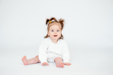 a baby girl on a white isolated background, a small child in a white knitted sweater smiling, a place for text