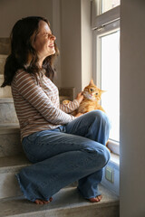 Brunette young woman playing with her rescue red cat at home. Copy space background.