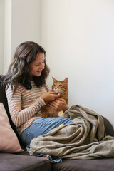Brunette young woman playing with her rescue red cat at home. Copy space background.