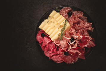 Cold cuts, appetizer, prosciutto, salami and ham, with maasdam cheese and olives, on a round plate, breakfast, top view, close-up, deserted