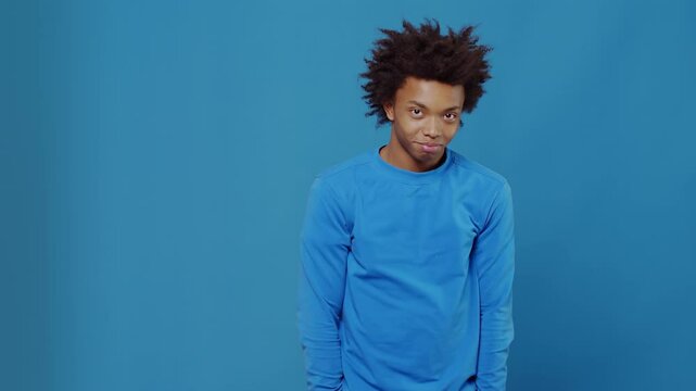 Confused young man shrugging in front of blue background