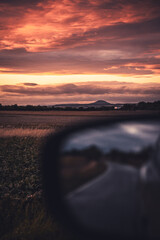 A beautiful sunset is mirrored in the rear view mirror of a car