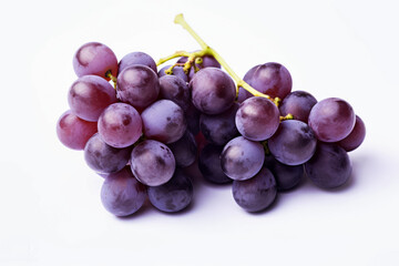 Bunch of purple grapes are sitting on a white background. The grapes are clustered together and appear to be ripe. Concept of abundance and freshness, as the grapes are a healthy