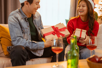happiness, party, happy, xmas, gift, friends, husband, together, togetherness, giving. A man and woman are sitting on a couch, holding presents and glasses of wine. They are smiling.