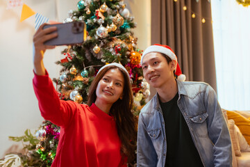 couple, surprise, romantic, present, festive, merry, gift, christmas, christmas eve, santa. A man and a woman are taking a selfie in front of a Christmas tree. They both have a smile on their faces.