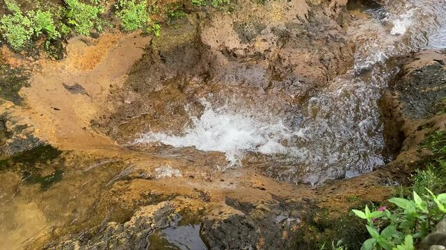 Close up view of river currents or water ripples. Clear fresh water flowing on the small ditch with green leaves plants, rocks and nature surrounding