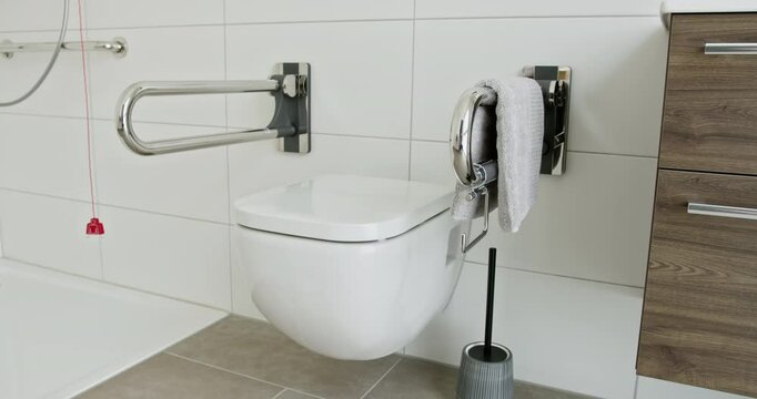 Modern bathroom featuring wall-mounted toilet, safety support bars, and towel. Accessible and functional design promoting independence and safety. Bathroom with safety support bars and toilet