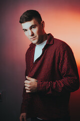 A man in a red plaid shirt is standing in front of a wall
