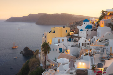 A picturesque sunset view over the iconic white-washed buildings and blue-domed churches of Oia, Santorini, overlooking the Aegean Sea.