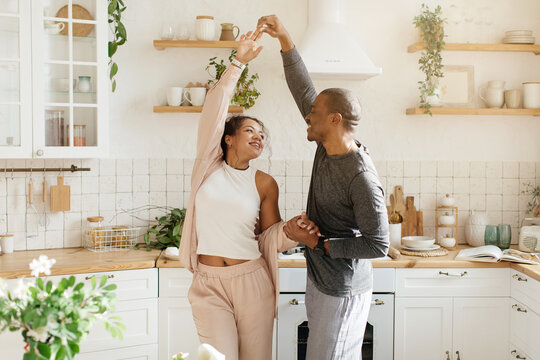 Happy African American young couple dancing in kitchen, having fun, overjoyed family celebrating relocation or anniversary, excited wife and husband moving to favorite music. High quality photo