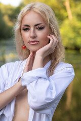 Naklejka premium Portrait of a young beautiful blonde girl in a white shirt near the river.