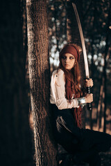 Outdoor portrait of young female in pirate costume holding a sword. Halloween