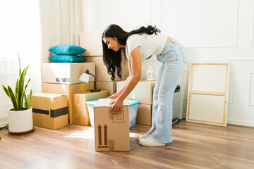 Latin woman showing an incorrect way of lifting a heavy box while moving into a new home