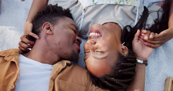 Above, black couple and kiss for picnic on grass with romantic date, love and food basket of anniversary. Smile, people and laughing with comic affection, relationship bonding and commitment outdoor