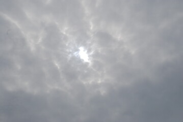 Gloomy sky above. Summer day, the sky is completely covered with heavy clouds, they are gray with white streaks. In the middle there is a bright spot through which bright light from the sun is visible