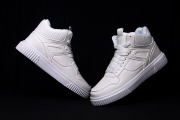 Pair of white fashion high top sneakers leaning on each other on black background
