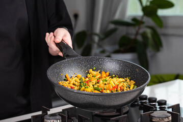 Close up of Chef cook hands cooking and toss roasted pasta, onion, pepper, carrot, vegetables, mushrooms, green peas, beans, garlic in frying wok pan on gas stove. Flying food levitation.