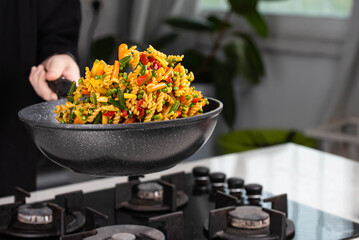 Close up of Chef cook hands cooking and toss roasted pasta, onion, pepper, carrot, vegetables, mushrooms, green peas, beans, garlic in frying wok pan on gas stove. Flying food levitation.