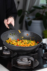 Close up of Chef cook hands cooking and toss roasted pasta, onion, pepper, carrot, vegetables, mushrooms, green peas, beans, garlic in frying wok pan on gas stove. Flying food levitation.