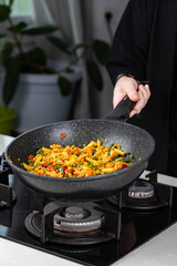 Close up of Chef cook hands cooking and toss roasted pasta, onion, pepper, carrot, vegetables, mushrooms, green peas, beans, garlic in frying wok pan on gas stove. Flying food levitation.