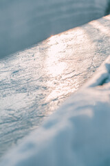 Close-up of smooth, sunlit ice surface on a skating rink with subtle grooves, creating a serene winter scene with soft light and frosty texture.
