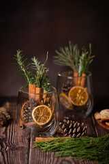 Christmas table decoration - pine cones, cinnamon sticks, pine and dried oranges in a glass on dark background 