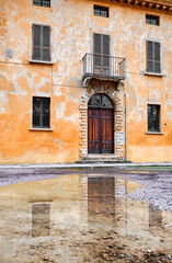 The facade of an ancient house with its peeling plaster and its reflection in the water in Brescia, Italy