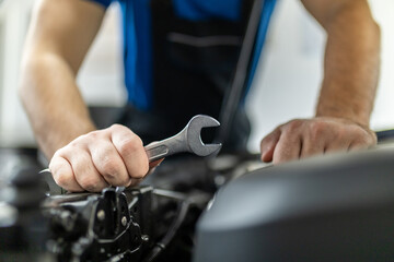 A mechanic works diligently on a vehicle engine with a wrench in a modern auto repair shop during daylight hours