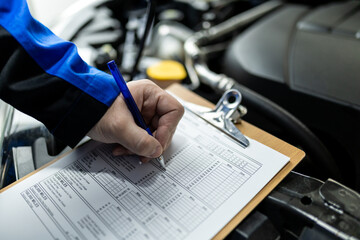 Mechanic inspecting vehicle using checklist while working in an auto repair shop during daylight hours