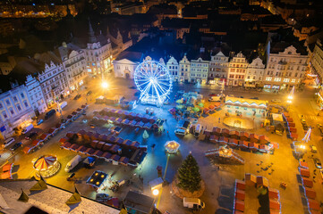 An aerial night shot of the Christmas markets in the square in Pilsen, featuring vibrant stalls surrounding the plaza and a large Ferris wheel lighting up the festive scene