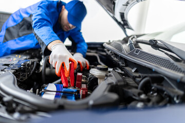 Mechanic jump-starting a vehicle battery in a garage during daytime using jumper cables to restore...