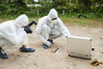 Two people wearing protective suits working at crime scene taking photographs and gathering evidence, copy space