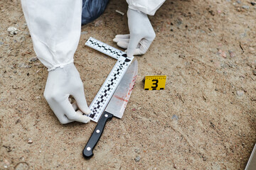 Top view closeup of unrecognizable person putting measuring tape next to evidence while marking...