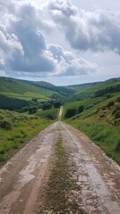 Naklejka premium Winding gravel road meandering through a picturesque countryside landscape surrounded by rolling green hills distant mountains and a dramatic cloudy sky