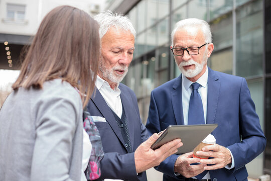 Small mixed group of senior businessmen and young woman having informal meeting on a sidewalk in front of an office building