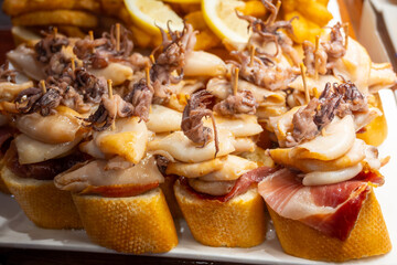 Fototapeta premium Typical snacks of Basque Country, pinchos or pinxtos skewers with small pieces of bread, fish, sea food, sweet green pepper served in bar in San-Sebastian or Bilbao, Spain