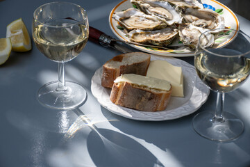 Plate with fresh live oysters with citron, bread, butter and white wine served at restaurant in oyster-farming village, Arcachon bay, Gujan-Mestras port, France