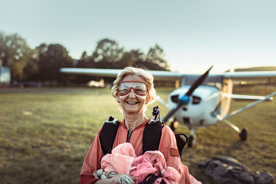 Senior woman smiling after skydiving with airplane in background