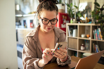 Young woman using smartphone and laptop at home workspace